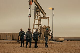 Oil-field crew walking near a pumpjack in Landman