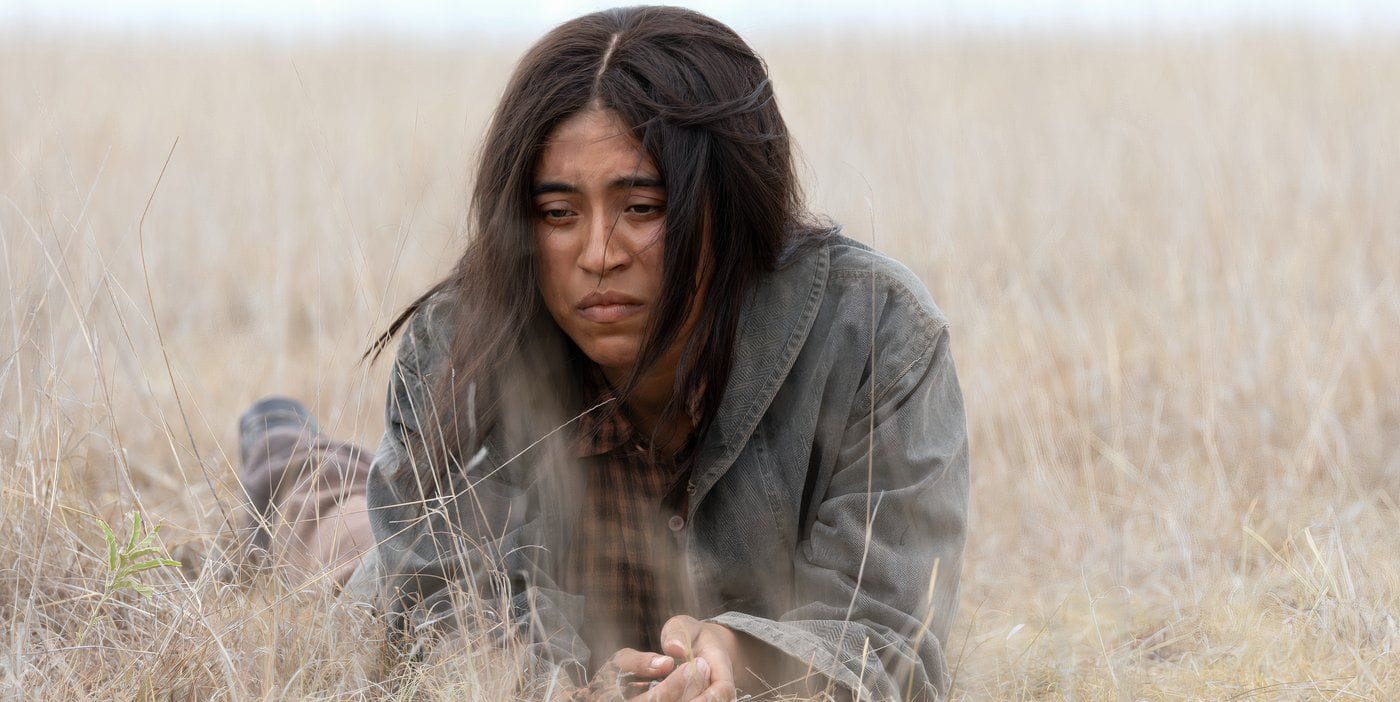 Aminah Nieves as Teonna Rainwater lying in the dry grass in 1923 Season 2 — she loses everything but rides west toward California in the finale. (Image: Paramount+/Screen Rant)